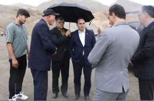 مدیرکل صمت آذربایجان غربی در حالی که فردی چتر بر سر او گرفته و دستانش در جیب است.